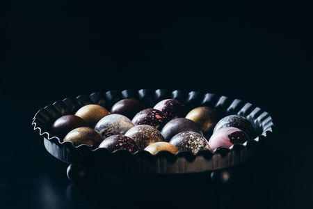 pile of different chocolate candies in bowl on black backgroundの写真素材