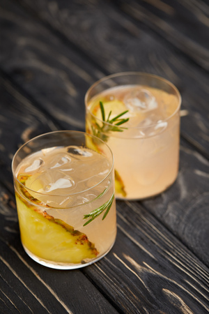 two glasses of lemonade with pineapple pieces, ice cubes and rosemary on grey wooden tabletopの写真素材
