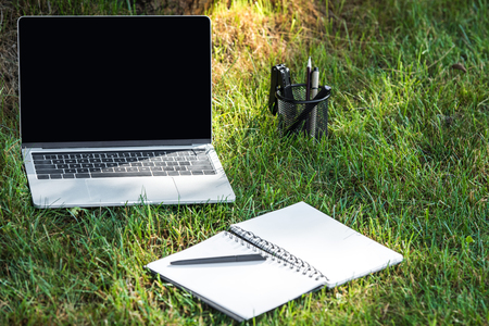 close up view of laptop with blank screen and empty textbook with pen on grass outdoors