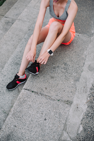 partial view of athletic girl tying laces on sports shoes while sitting on stairsの写真素材