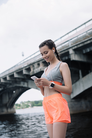 beautiful young sportswoman using smartphone with earphones and smartwatchの写真素材