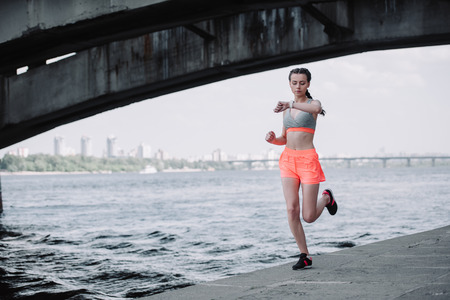 sportswoman looking at smart watch while jogging on quay