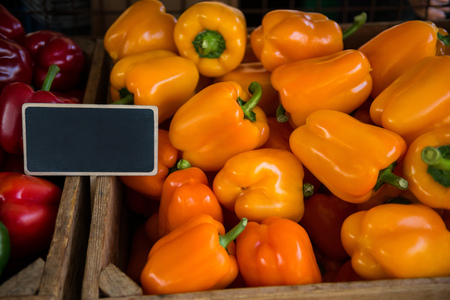 close up view of red and yellow bell peppers with blank signobardの写真素材