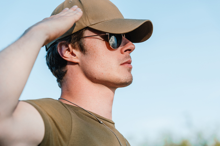 side view of young soldier in cap and sunglasses against blue skyの写真素材