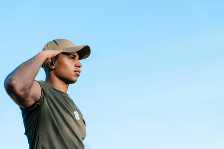side view of african american soldier in cap with tag dog against blue skyの写真素材