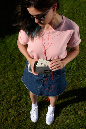 high angle view of stylish young woman in sunglasses and earphones with retro audio cassette and...