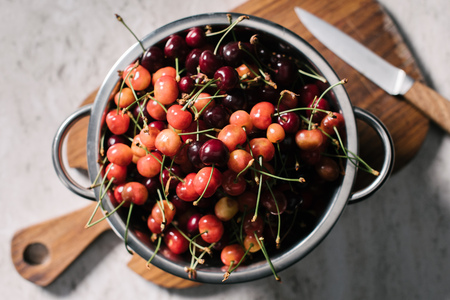 top view of metallic pan with ripe sweet cherries on wooden cutting board with knife
