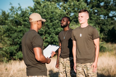 african american tactical instructor with notepad and young multiracial soldiers in military uniform...