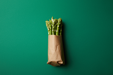 top view of bunch of ripe asparagus covered with kraft paper on green surfaceの写真素材