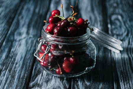 close-up view of ripe sweet healthy cherries in glass jar on wooden tableの写真素材