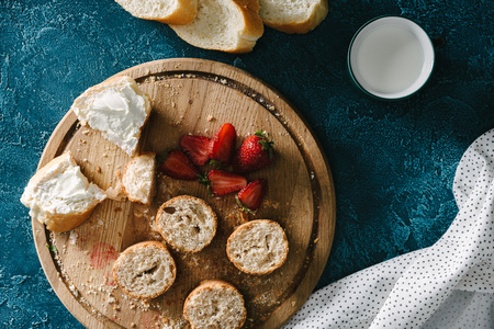 Cutting board with strawberries and sandwiches with cream cheese on blue tableの写真素材
