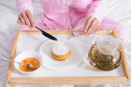 partial view of woman in pajamas having pancakes with jam for breakfast in bed at homeの写真素材