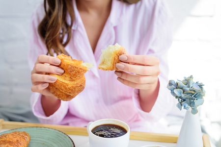 partial view of woman in pajamas having croissant and coffee for breakfastの写真素材