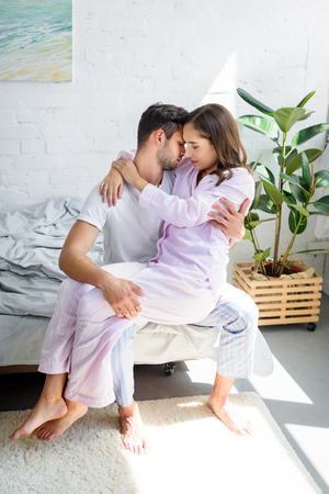 young tender woman sitting on knees of her boyfriend and hugging him on bedの写真素材