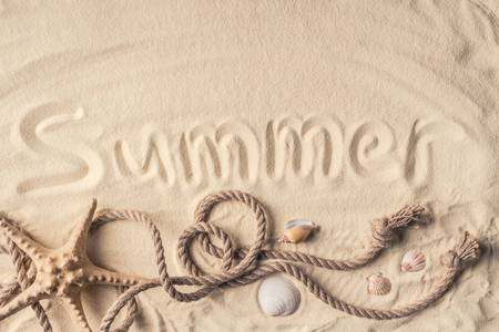 Starfish and shells with rope on light sand with summer inscriptionの写真素材