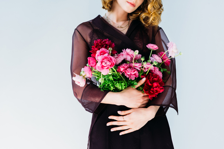 cropped shot of elegant stylish woman holding tender pink flowers isolated on greyの写真素材