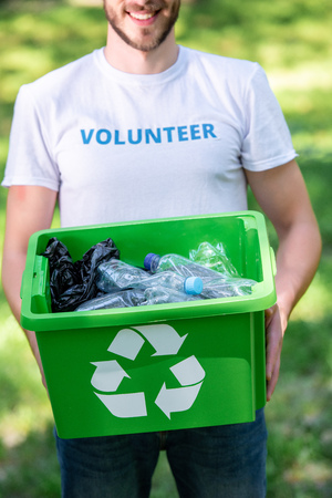 partial view of smiling volunteer holding recycling box with plastic wasteの写真素材