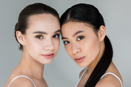 portrait of two attractive multicultural women isolated on gray backgroundの写真素材