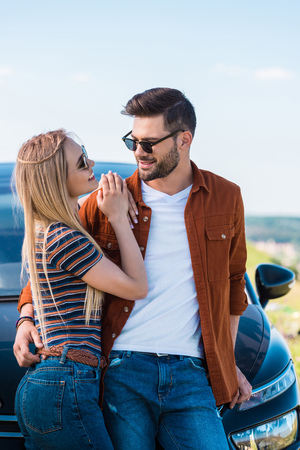 smiling stylish couple in sunglasses standing near carの写真素材