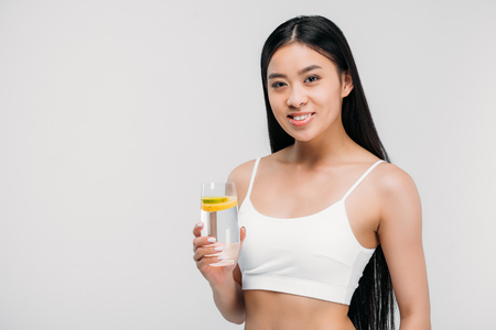 elegant asian girl in bra holding glass of water, isolated on greyの写真素材