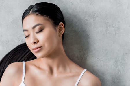pretty brunette asian girl with closed eyes, on greyの写真素材