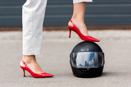cropped image of woman in red high heels putting leg on motorcycle helmet on streetの写真素材