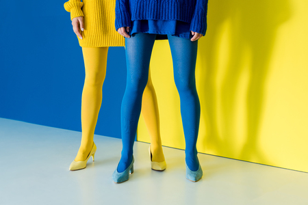 Cropped view of women wearing blue and yellow pantyhose on blue and yellow backgroundの写真素材