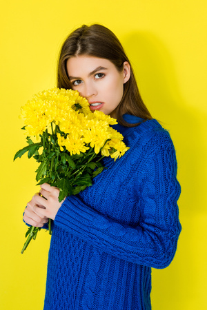 Beautiful brunette girl holding bouquet of yellow chrysanthemums on yellow backgroundの写真素材