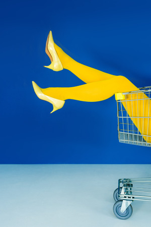 Cropped view of female legs in shopping cart on blue backgroundの写真素材