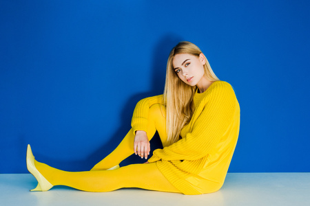 Female fashion model dressed in yellow sitting on floor on blue backgroundの写真素材