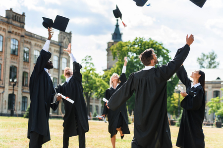 young graduated students throwing up graduation caps in university gardenの写真素材