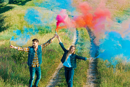 high angle view of young couple holding colorful smoke bombs on rural meadowの写真素材