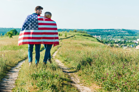 rear view of young couple with american flag on rural meadow, independence day conceptの写真素材
