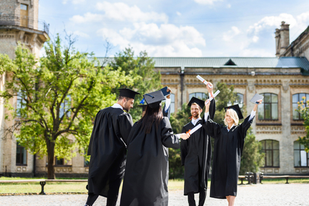 young graduated students with diplomas greeting each other in college gardenの写真素材