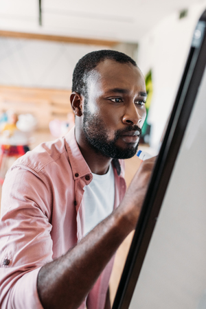 concentrated young african american man writing on whiteboardの写真素材