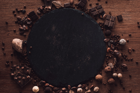 elevated view of cutting board surrounded by various types of chocolate pieces, truffles. coffee grains and cocoa beans on wooden tableの写真素材