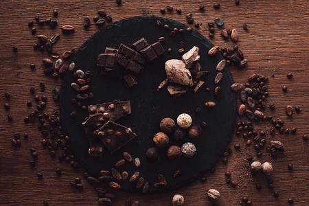 elevated view of cutting board with various types of chocolate pieces and truffles surrounded by cocoa beans, coffee grains and nutmegs on wooden tableの写真素材