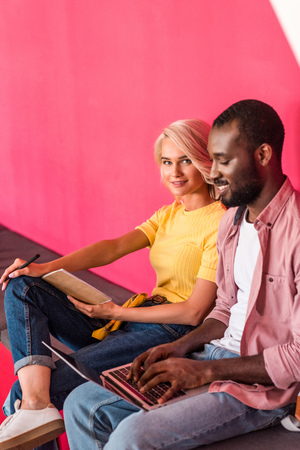 young students working with laptop while sitting under red wallの写真素材