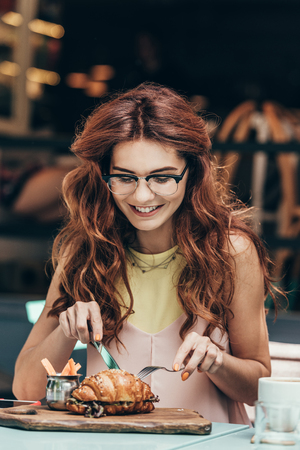 portrait of smiling woman in eyeglasses having breakfast alone in cafeの写真素材