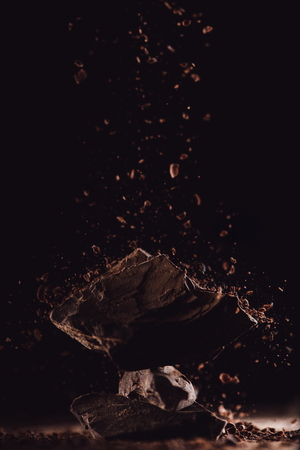 closeup shot of grated chocolate falling on pieces of chocolate on black backgroundの写真素材