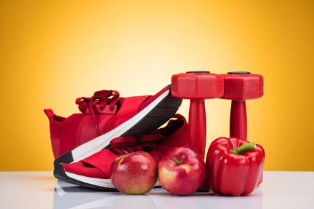 close-up view of red sneakers, apples, pepper and dumbbells on yellowの写真素材