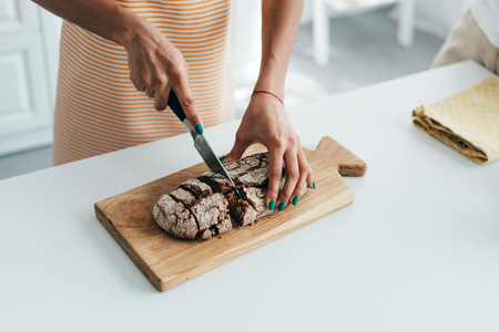cropped shot of woman cutting bread on board at kitchenの写真素材