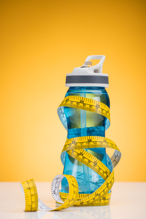 close-up view of sports bottle with water and measuring tape on yellowの写真素材