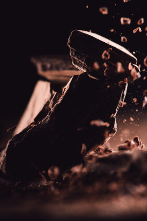 close up view of grated dark chocolate falling on pieces of chocolate on black backgroundの写真素材