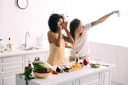 young man taking selfie on smartphone with girlfriend covering eyes by cherry tomatoesの写真素材