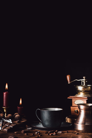 closeup shot of cup of coffee at wooden table with chocolate, truffles, coffee grains, candles and turk on black backgroundの写真素材