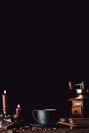 close up view of cup of coffee at wooden table with chocolate, truffles, coffee grains and candles on black backgroundの写真素材