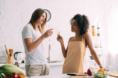 multicultural young couple clinking wine glasses at kitchenの写真素材
