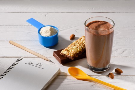 close-up shot of sports nutrition and notepad with be fit sign on white wooden table