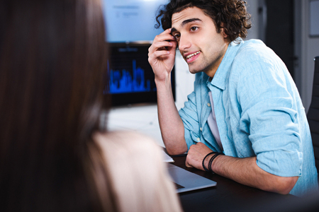 young businessman sitting at table with laptop and talking to partner at modern officeの写真素材